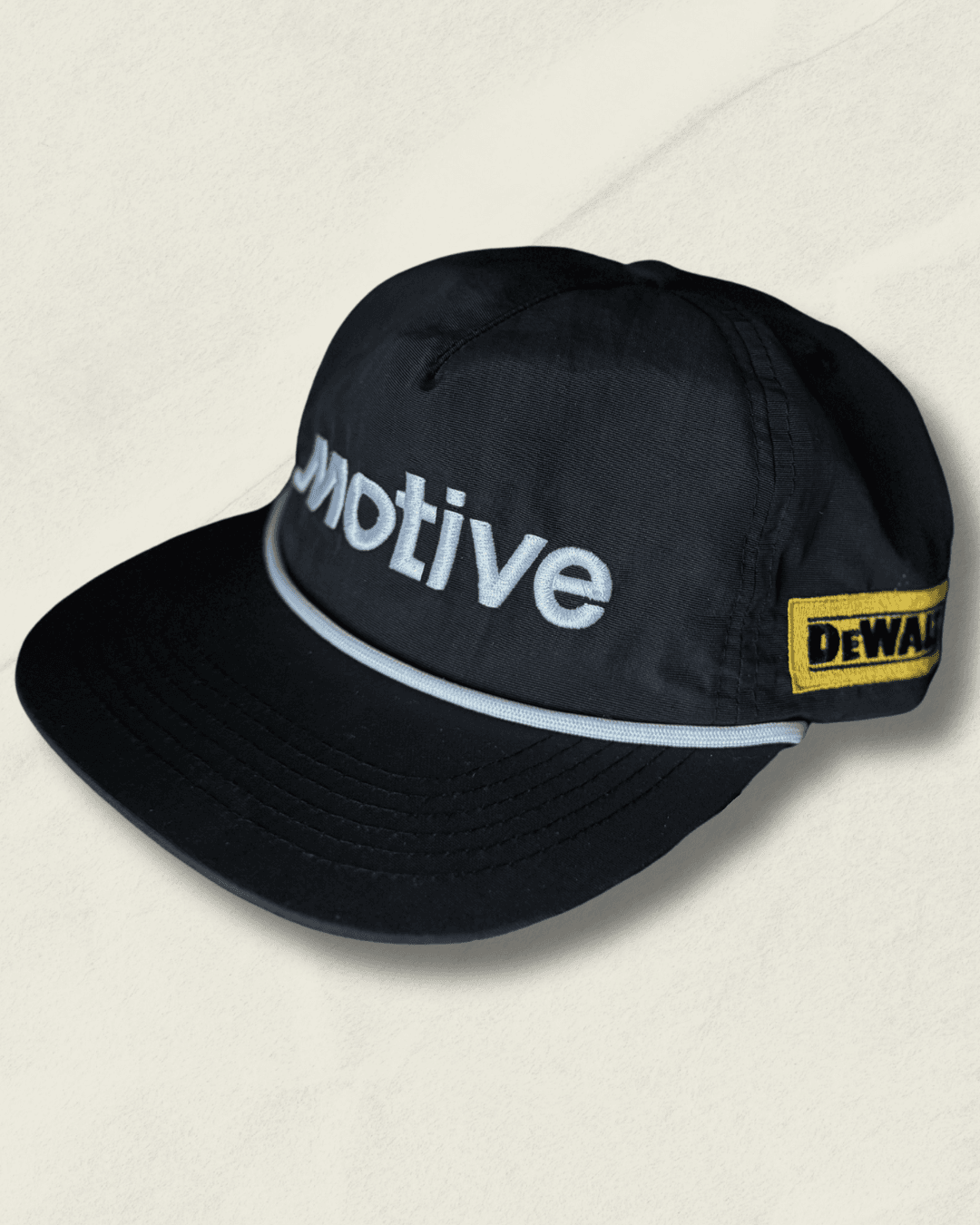 Black Malbon Golf x Motive x DeWalt nylon rope golf hat, front view with raised white motive embroidery, white rope, and yellow DeWalt patches on the sides.